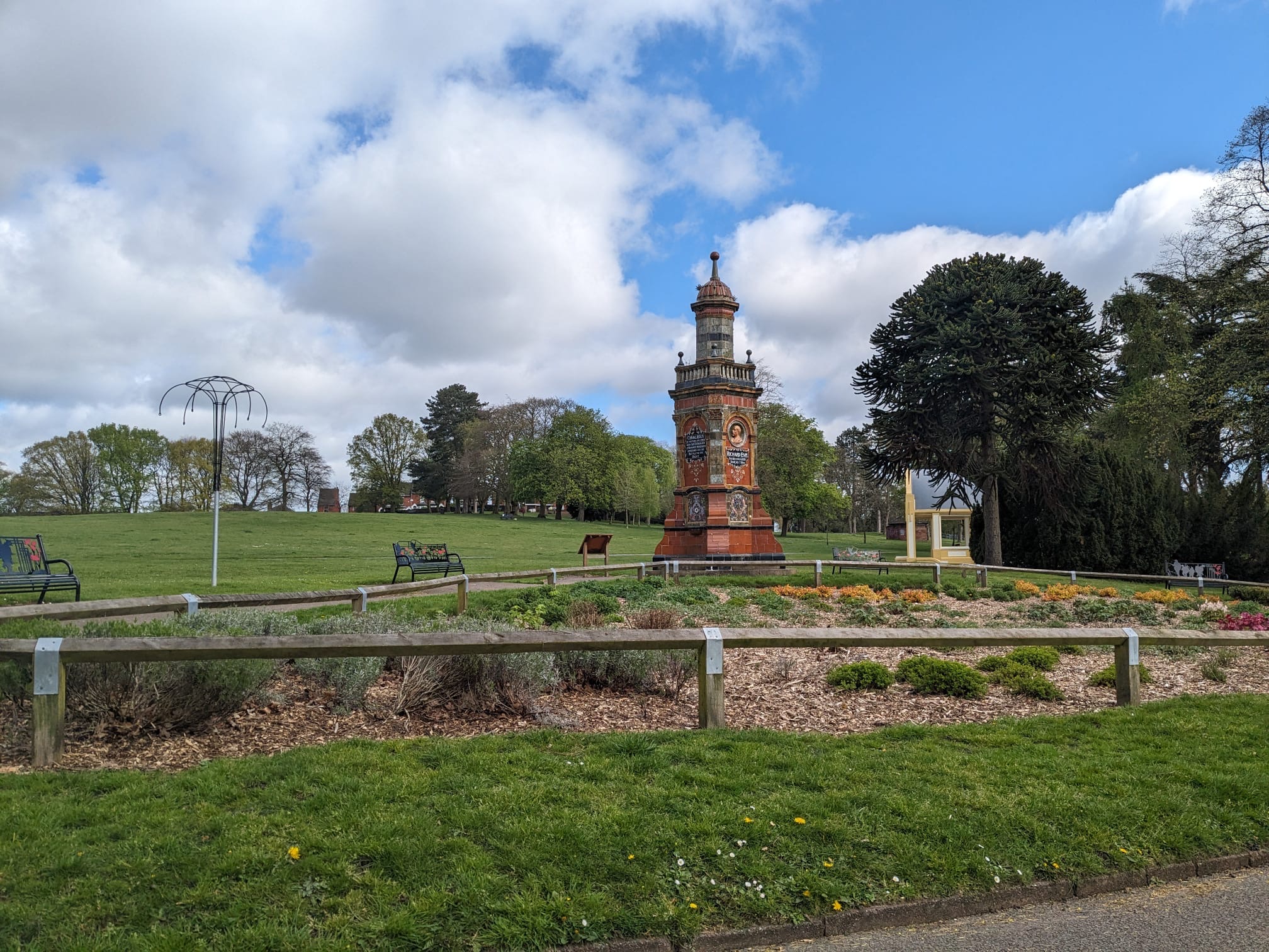 red tile memorial tower in park with flower bed in foreground